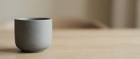 Minimalist gray ceramic cup on wooden table with soft neutral background, suitable for home decor and lifestyle design projects.