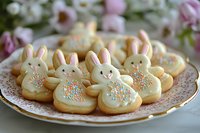 Easter bunny sugar cookies decorated with white frosting and colorful sprinkles arranged on vintage plate with pink floral background, festive spring holiday baking treats.