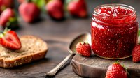 Fresh strawberry jam in glass jar on rustic wooden board with whole berries and slice of bread, homemade preserves in natural morning light.