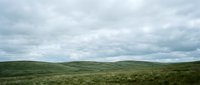 Rolling green hills under dramatic cloudy sky, vast open moorland landscape with sparse vegetation, suitable for nature, travel, and environmental design projects.