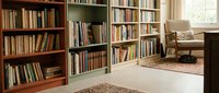 Cozy home library interior with wooden bookshelves filled with books, comfortable reading chair and warm natural lighting creating peaceful study atmosphere.