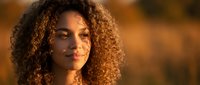 Young mixed-race woman with curly hair in warm golden sunlight, natural beauty portrait for lifestyle and wellness content.