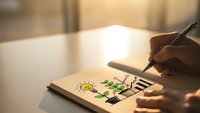 Hand drawing colorful environmental icons in notebook with pen on wooden desk, showcasing green energy concepts and sustainability planning for eco-friendly projects.