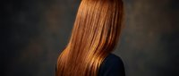 Woman with long straight glossy auburn hair seen from behind against dark studio background, showcasing healthy shiny red hair care concept.