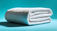 Folded white soft fleece blanket on turquoise background with shadow, cozy home textile for comfort and warmth.