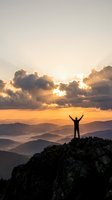 Silhouette of victorious hiker with raised arms standing on rocky mountain peak at golden sunrise overlooking misty valley layers and dramatic cloudy sky.