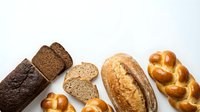 Assorted fresh baked bread loaves and rolls arranged on white background, including whole wheat, rye, sourdough and braided varieties for bakery and food styling.