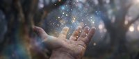 Open palm releasing magical golden sparkles and light particles into dreamy bokeh background creating mystical atmosphere for spiritual wellness concepts.