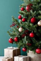 Decorated Christmas tree with red and gold ornaments, berries, and wrapped gifts against teal wall background.