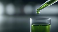 Green liquid dropping from glass pipette into laboratory test tube against blurred background, scientific research concept in modern lab setting.