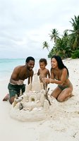 Family building sandcastle on tropical beach with turquoise water and palm trees. Parents and young child enjoying summer vacation activities together on sandy shore.
