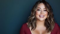Young Caucasian woman with wavy brown hair smiling warmly at camera wearing burgundy top against dark teal background for portrait photography.