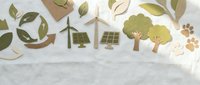 Eco-friendly paper cut elements featuring wind turbines, solar panels, trees, and recycling symbols arranged on white linen background.