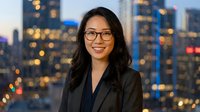 Professional Asian businesswoman with glasses smiling confidently against city skyline at dusk for corporate headshots and business presentations.
