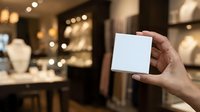 Close-up of hand holding blank white card in luxury jewelry store with bokeh background, suitable for business cards, gift cards, promotions.