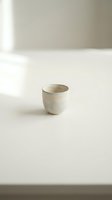 Minimalist ceramic cup on white surface with soft natural lighting for modern interior design and lifestyle photography.