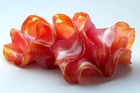Thinly sliced prosciutto ham arranged in delicate folds creating waves of pink and orange hues against white background, showcasing fresh cured meat texture.