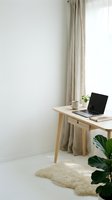 Minimalist workspace with wooden desk, laptop, notebook, and potted plant by window with beige curtains, bright natural light, and cream rug for home office design.