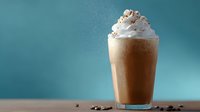 Creamy chocolate milkshake topped with whipped cream and cocoa powder in glass against turquoise background with coffee beans scattered on surface.