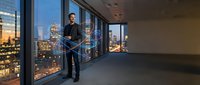Businessman in dark suit standing in modern high-rise office with floor-to-ceiling windows overlooking illuminated cityscape at dusk, suitable for corporate, leadership, and business success concepts.