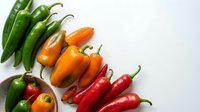 Fresh green and red chili peppers, orange bell peppers arranged on white background. Colorful hot spices for cooking, food photography, culinary ingredients, recipe illustration, kitchen design.