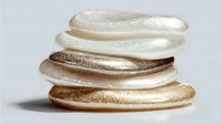 Stack of shimmering cream and bronze eyeshadow swatches on gray background, showcasing metallic makeup textures for cosmetic advertising.