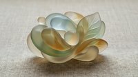 Translucent glass sculpture with flowing organic curves in soft green and amber tones on neutral background for modern interior design and artistic decoration.