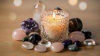 Healing crystals and gemstones arranged around glowing candle in ornate glass holder creating peaceful meditation and wellness atmosphere for relaxation.
