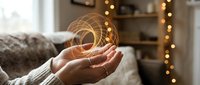 Hands holding glowing golden spiral energy symbol in cozy living room with warm lights creating magical atmosphere for wellness and spiritual concepts.