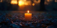 Glowing candle flame illuminates fallen autumn leaves at sunset, creating atmospheric mood with golden bokeh and dark blue tones in forest setting.
