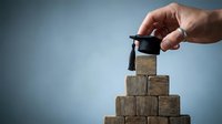 Hand placing graduation cap on wooden blocks pyramid representing education achievement and career advancement success.