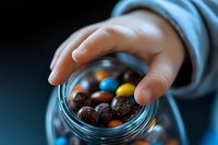 Child hand reaching for colorful chocolate candies in glass jar, tempting sweet treats and childhood indulgence concept for parenting and nutrition themes.