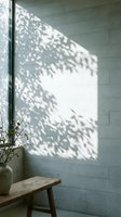 Sunlight streaming through foliage casts dappled shadows on a pale brick wall beside a wooden bench with potted plant, creating natural light patterns for interior design and architectural projects.