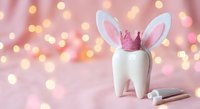 Tooth fairy concept with white molar wearing bunny ears and crown on pink background with bokeh lights for dental care and children fantasy themes.
