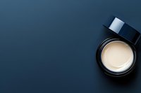 Open luxury face cream jar with lid on dark navy blue background, top view flat lay skincare cosmetic product.