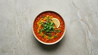 Traditional Middle Eastern shakshuka with poached eggs in spicy tomato sauce garnished with fresh herbs served in rustic ceramic bowl on marble surface.