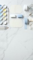 Watercolor painting supplies arranged on marble surface with brushes, paints, paper, ribbons and glass jars for artistic projects and creative workshops.