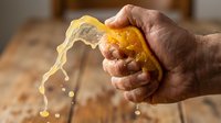 Hand squeezing fresh lemon, juice dripping from citrus fruit over wooden surface, food preparation and cooking ingredient.