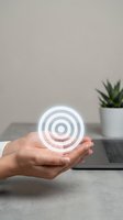 Hands holding glowing target symbol above laptop representing business goals, strategy planning and achievement in modern workspace.