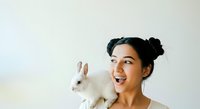 Young woman with dark hair styled in buns, smiling brightly while holding a white rabbit against her chest. Isolated on white background for design use.