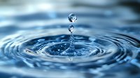Crystal clear water drops creating concentric ripples on blue water surface with suspended droplets caught in mid-air showing surface tension and splash dynamics.