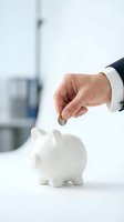 Businessman hand inserting coin into white piggy bank on office desk for savings and investment planning concepts.