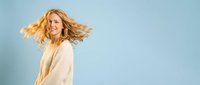 Happy blonde woman with flowing hair in beige sweater against blue sky background expressing joy and freedom in natural outdoor portrait.