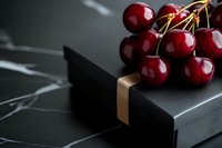 Fresh red cherries with stems on elegant black marble surface with gold accent for gourmet food photography and luxury culinary presentations.