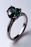 Heart-shaped emerald green gemstone engagement ring in black rhodium plated setting against light background, showcasing luxury jewelry design.