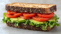 Fresh lettuce and juicy tomato slices layered between dark multigrain bread create appetizing vegetarian sandwich on light background, ready for healthy lunch.