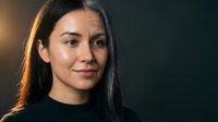 Young Hispanic woman with long dark hair in black top against dark background with warm lighting for portrait photography and commercial use.