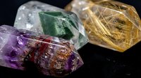Collection of raw healing crystals including amethyst, green fluorite and rutilated quartz gemstones on dark surface for spiritual wellness and meditation practices.