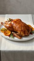 Golden roasted whole chicken garnished with fresh herbs and orange slices on white plate, ready for holiday dinner or special occasion meal.