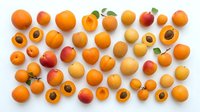 Apricots and peaches arranged flat lay on white background, whole and halved fruits showing pits and flesh, suitable for food photography, culinary design, nutrition content.